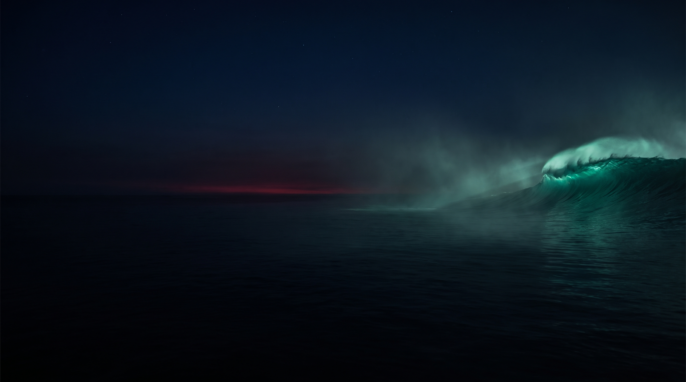 A vast calm dark ocean at night with a single enormous wave rising on the right, its crest glowing emerald teal through mist, and a thin crimson glow on the horizon